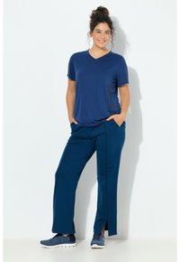 Marineblaues V-Ausschnitt-T-Shirt mit floralem Muster an der Seite, kombiniert mit passenden marineblauen Sporthosen mit Seitenschlitzen, getragen mit blauen Turnschuhen.