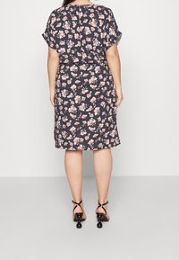 Kukkamekkona tummansinisellä pohjalla, jossa on vaaleanpunaisia ja valkoisia kukkia, lyhyet hihat, polvipituinen, valmistettu kevyestä kankaasta, yhdistettynä mustiin korkokenkiin.