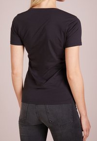 Camiseta negra de manga corta hecha de algodón, con un diseño ajustado y cuello redondo. Se lleva con jeans ajustados grises, que muestran una textura suave.