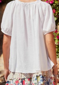 White, loose-fitting top with puffed sleeves and elastic neckline, paired with a floral-patterned, layered skirt featuring lace trim.