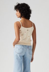 Beige strikket top med tynde stropper, prydet med farverig stjernebroderi og en ribbet nederkant. Kombineret med lyseblå brede jeans.