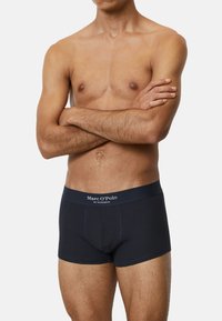 Mörkblå boxerkalsonger i ribbat tyg med en logoband i midjan. Designen inkluderar en stödjande framficka och en åtsittande siluett.