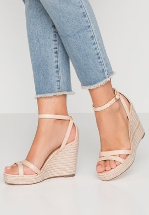 Sandalias de cuña color nude con tiras cruzadas, tacón de cuña tejido en rafia y cierre con hebilla en el tobillo. Combinadas con jeans vaqueros azules recortados.