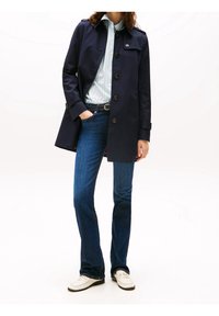 Abrigo tipo gabardina azul marino con cierre de botones, camisa de rayas azul claro, vaqueros acampanados azul oscuro y mocasines blancos. Tejido liso y diseño cl�ásico.