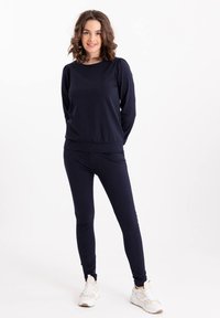 Marineblauwe sweatshirt met lange mouwen en ronde hals, gecombineerd met bijpassende slim-fit broek. Materiaal lijkt zacht, gestructureerd en comfortabel te zijn.