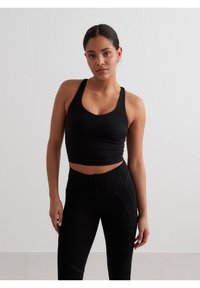 Juodas prigludęs sportinis liemenukas su apvaliu iškirpimu. Sklandžiai audiniai ir lenkto nugaros dizainas. Derinamas su aukštu liemeniu juodomis legginomis, turinčiomis panelių detalių.