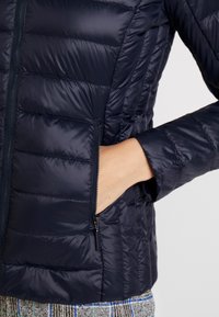 Navy puffer jacket with horizontal quilted pattern, zippered hand pocket, and a stand collar. Smooth, lightweight material and fitted cuffs.