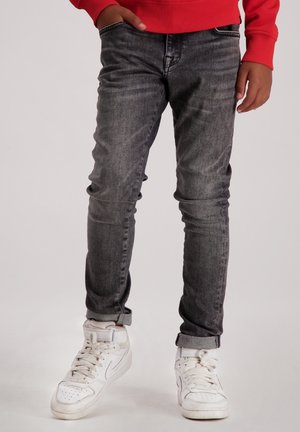 Grijze denim jeans met een slim fit, voorzien van lichte slijtageplekken, opgerolde broekspijpen en een versleten textuur, gecombineerd met witte high-top sneakers.