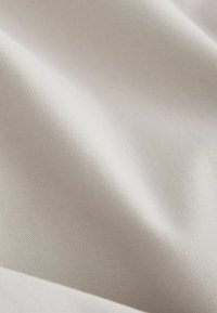 Tissu lisse de couleur ivoire avec de fines côtes diagonales et de doux pliages créant des ombres délicates sur la surface.