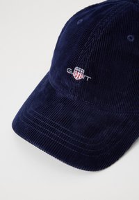 Gorra de algodón en relieve color marino con visera curva y logotipo bordado de GANT. Presenta un tejido texturizado y seis orificios de ventilación en la corona.