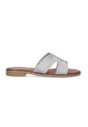 Sandalias deslizantes de tela plateada con suela plana, diseño de tiras cruzadas y tachuelas decorativas a lo largo del borde. La plantilla interior es marrón.