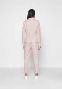 Ljusrosa kostym med små orange prickar, bestående av en skräddarsydd jacka och slim-fit byxor. Slät textur; matchad med vita sneakers.