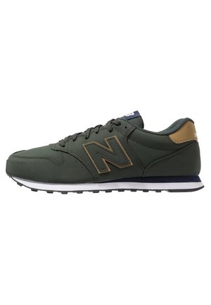 Dark green New Balance sneaker with brown accents, black laces, white midsole, and treads on the black outsole, viewed from the side.