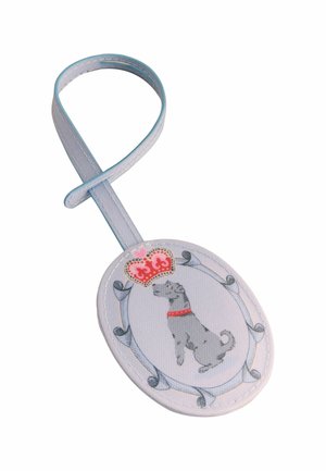 Oválny biely cestovný štítok so sivým psom, ktorý má na krku červený obojok a nad ním červenú korunu, pripevnený na bielom remienku.