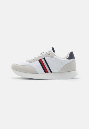 Zapatilla blanca con acentos de ante gris, detalles a rayas en rojo y azul marino, cierre con cordones y suela de goma texturizada. Diseño atlético clásico.