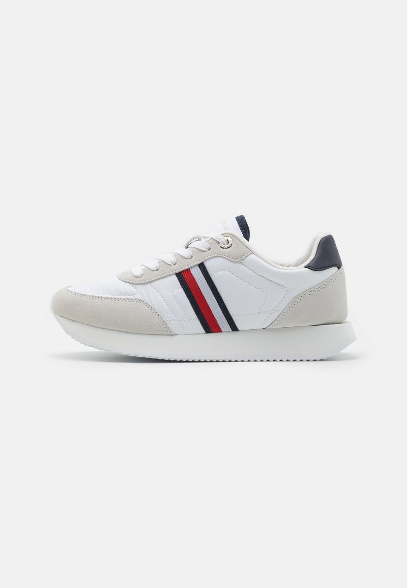 Zapatilla blanca con acentos de ante gris, detalles a rayas en rojo y azul marino, cierre con cordones y suela de goma texturizada. Diseño atlético clásico.
