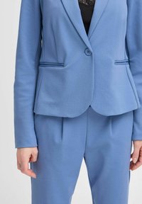 Blazer ajusté bleu clair avec un bouton unique, revers crantés, deux poches avant et tissu lisse, associé à un pantalon fuselé assorti.
