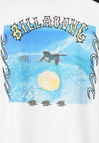 Hvid bomulds T-shirt med et grafisk design af en surfer på en bølge med en gul sol, omkranset af blomsterdetaljer og teksten "BILLA".