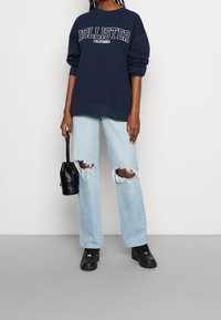 Granatowa bluza z napisem "Hollister California", jasnoniebieskie podniszczone dżinsy z podartymi kolanami, czarna torebka i czarne trampki.