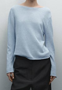 Light blue knit sweater with a wide neckline and long sleeves, paired with dark trousers. Smooth texture and relaxed fit.