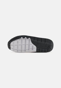 Mustvalge tennisekingade põhi, millel on tekstuuriga kummist haardepind, paindlikud sooned ja küljel graveeritud bränding.