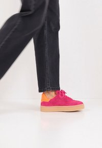 Φωτεινά ροζ πάνινα παπούτσια από σουέτ με πορτοκαλί λεπτομέρεια στη φτέρνα, με υφή επιφάνειας και λεπτά κορδόνια, συνδυασμένα με μαύρο τζιν.