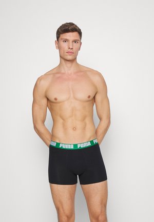 Schwarze Boxer-Briefs mit einem grünen PUMA-Logo auf dem elastischen Bund, passgenaues Design und glatte Textur. Getragen von einem männlichen Modell.