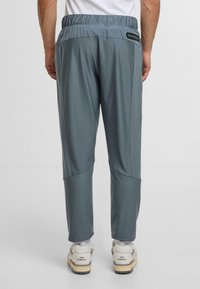 Herrarnas ljusgrå träningsbyxor med en slät yta, elastisk midja, sidofickor med dragkedja och smalnande fållar. Bärs med vita och beige sneakers.