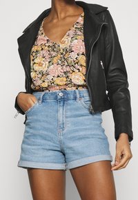 Černá kožená motorkářská bunda přes vršek s květinovým vzorem růžových a žlutých květin, doplněná světlými modrými džínovými šortkami s ohrnutými lemy.