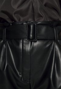 Ceinture en cuir noir avec une boucle rectangulaire, portée sur un haut sombre à texture lisse. La ceinture présente des coutures visibles et une finition brillante.