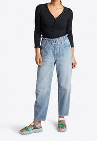 Schwarzes, geripptes Langarmoberteil, hellblaue Jeans mit hoher Taille und elastischem Bund sowie mehrfarbige flache Sandalen mit strukturiertem Sohlen.