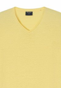 T-shirt giallo con scollo a V realizzato in morbido tessuto testurizzato. Presenta una vestibilità ampia e un delicato motivo mélange. Etichetta del marchio visibile all'interno dello scollo.