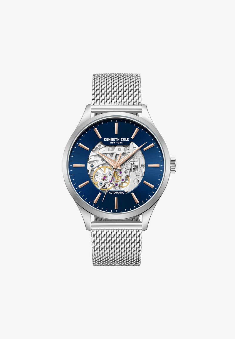 Automātiskie pulksteņi ar nerūsējošā tērauda korpusu, zilu ciparnīcu, sudraba acu jostu un atklātu mehānismu, kas demonstrē zobratus un purpura dārgakmeņus.