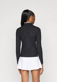 Maglia nera a maniche lunghe con motivo rigato testurizzato, colletto alto e design aderente, abbinata a una gonna a ruota bianca.
