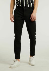 Zwarte slim-fit broeken, katoenmix, tailleband met riemlussen, ritssluiting, voorzakken, gecombineerd met witte sneakers. Glad textuur, zorgvuldig passend.