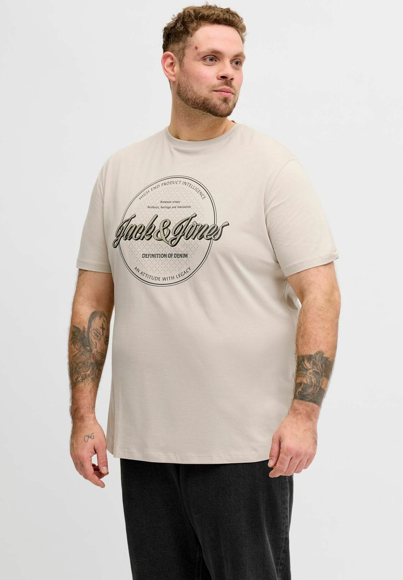 Lys beige bomuld T-shirt med korte ærmer. Har sort grafisk print med teksten "Jack & Jones" og en cirkulær ramme. Enkel design, afslappet pasform.