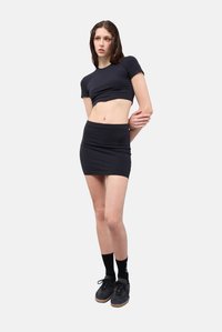 Cropped shirt nera e gonna mini abbinata realizzate in tessuto elasticizzato, abbinate a calzini e scarpe nere, creando un look monocromatico.