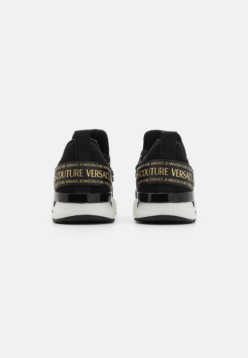 Czarne sneakersy z teksturową cholewką, z połyskującą czarną piętą, białą podeszwą i złotym detalem z brandingiem "VERSACE JEANS COUTURE".