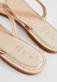 Sandali piatti in oro rosa metallico con cinturini sottili, soletta testurizzata e suola cucita. Presenta un logo del marchio impresso nella soletta.