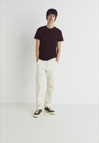 Dark burgundy t-shirt, white cargo pants with pockets, and brown sneakers. Simple design with a relaxed fit and minimal detailing.