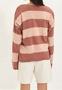 Pull en tricot avec de larges rayures horizontales en rose poussiéreux et rose clair. Texture douce, coupe décontractée et ourlet côtelé.