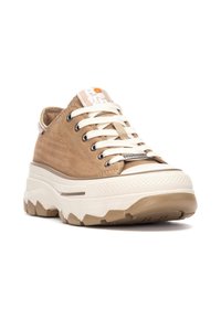 Zapatilla de lona beige con cordones blancos, suela de goma y plataforma texturizada. Presenta una etiqueta de logo en la lengüeta y detalles en contraste.