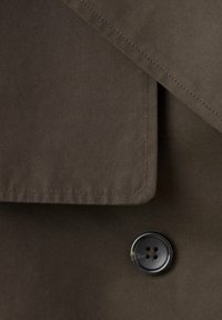 Gros plan d’un tissu marron avec des surpiqûres en couches et un seul bouton noir à quatre trous.