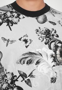 Μαύρο και άσπρο φούτερ με λουλουδάτο σχέδιο, με μαύρη πλεχτή λαιμόκοψη, που διαθέτει λεπτομερείς απεικονίσεις τριανταφυλλιών, πεταλούδων και διακοσμητικών στοιχείων.