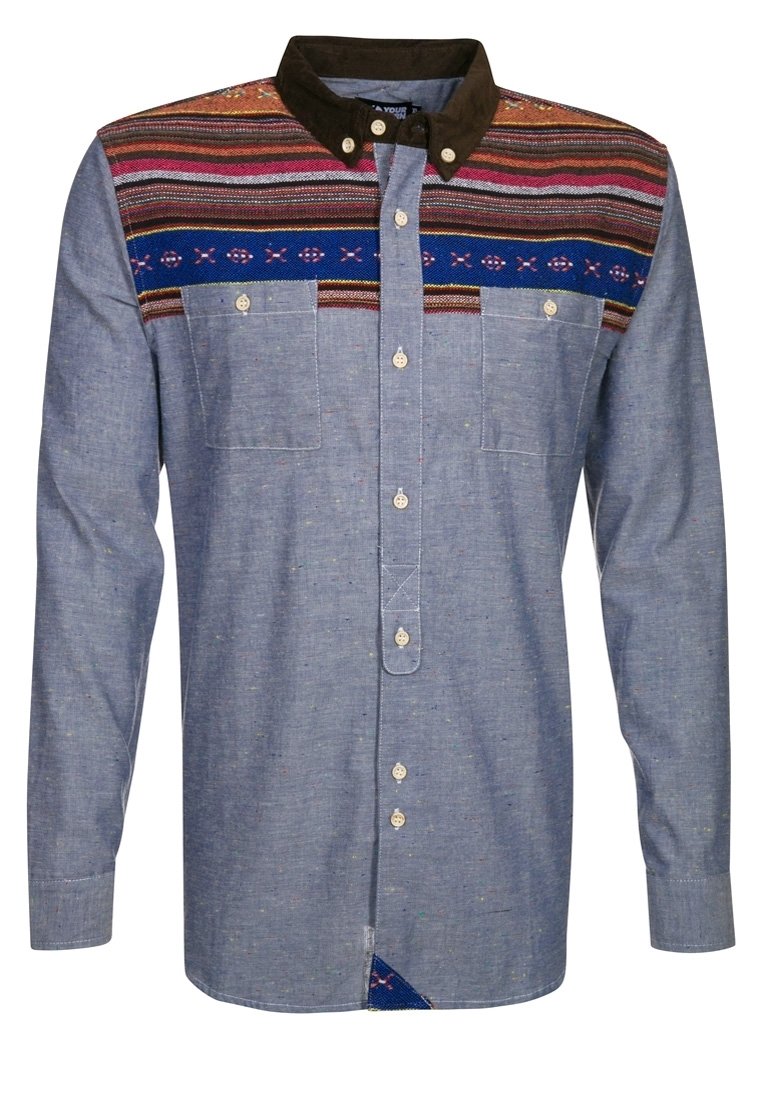 Camisa abotonada de tela chambray azul, con cuello marrón y tapeta con estampado que presenta rayas multicolores y diseños geométricos.