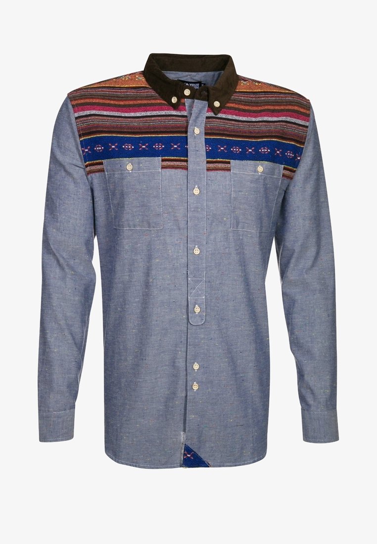 Camisa abotonada de tela chambray azul, con cuello marrón y tapeta con estampado que presenta rayas multicolores y diseños geométricos.