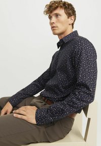 Marineblauwe shirt met lange mouwen, voorzien van een klein bloemenpatroon in beige en perzik. De stof heeft een soepele textuur en knoopmanchetten.