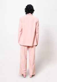 Rosa maßgeschneiderter Anzug mit einem boxy Blazer mit Reverskragen und weit geschnittenen Hosen, aus glattem Stoff mit matter Oberfläche.