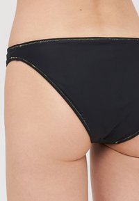 Crni donji dio bikinija s glatkom teksturom, s kontrastnim neon šavovima duž rubova. Klasični visoki kroj za minimalnu pokrivenost.