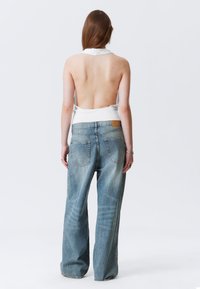 Weißes ärmelloses Top mit tiefem Rückenausschnitt, kombiniert mit hellblauen, weit geschnittenen Jeans aus Denim mit Gesäßtaschen und einem Leder-Label.